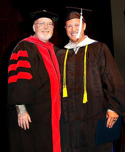 Graduate stands next to president Randy Roberts while holding his diploma.