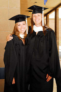 Two graduates smile while posing for a photograph.