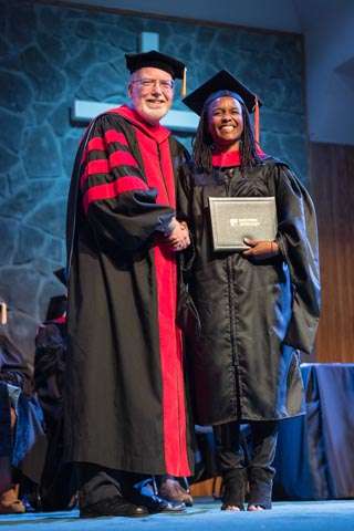 Graduate standing with diploma next to seminary president.