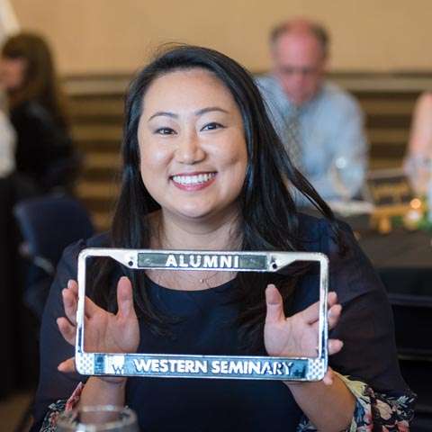 Graduate holding a frame that says "Alumni".